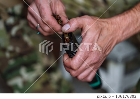 Hands loading ammunition into rifle magazine close up 136176802