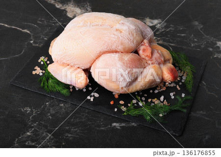 Whole frozen chicken on black slate board with salt and dill. Raw poultry carcass covered in ice crystals on dark marble background. Uncooked meat ingredient ready for defrosting. High quality photo 136176855