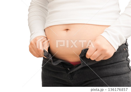 Overweight woman trying to button tight jeans. Cropped view of female belly with unzipped pants isolated on white background. Weight gain and obesity concept. High quality photo 136176857