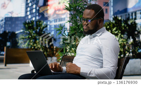 African american person frustrated and distressed working online from a bench, being displeased and disappointed with bad news on screen. Surrounded by skyscrapers in metropolitan area. Camera B. African american person frustrated and distressed working online from a bench, being displeased and disappointed with bad news on screen. Surrounded by skyscrapers in metropolitan area. Camera B. 136176930