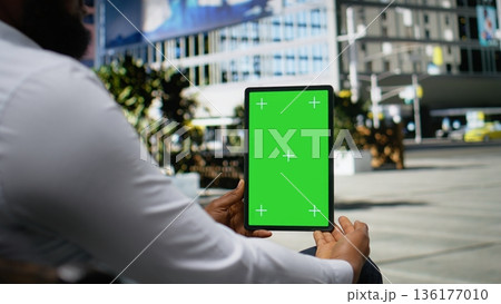 Vertical green screen with black man sitting relaxed on a bench, working online with his tablet near downtown city center. Street style and confident attitude in metropolitan life. Camera A. Vertical green screen with black man sitting relaxed on a bench, working online with his tablet near downtown city center. Street style and confident attitude in metropolitan life. Camera A. 136177010