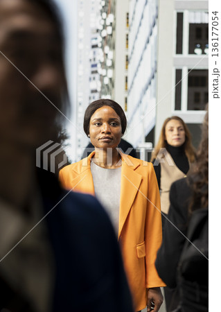 Black modern female professional walking on city street during daily commute, blurred motion of urban crowd reflecting realistic city life. Business lifestyle and metropolitan street life. Black modern female professional walking on city street during daily commute, blurred motion of urban crowd reflecting realistic city life. Business lifestyle and metropolitan street life. 136177054