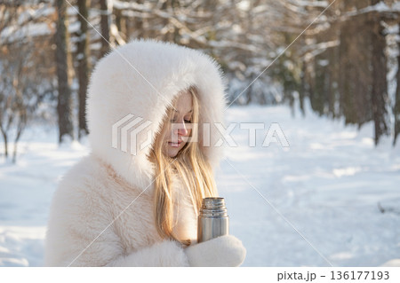Young woman drinking hot tea from thermos in winter park 136177193