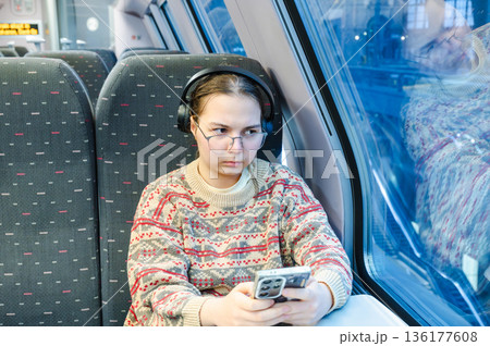 Smiling teenager girl with gallses and headphones in train 136177608
