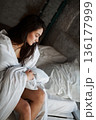 A woman with black hair wakes up in the morning in a white blanket and catches the rays of the sun. The portrait is creative, with brown eyes. High quality photo 136177999