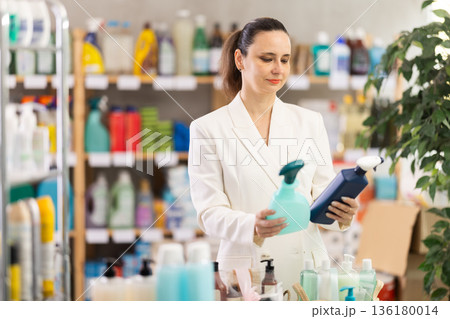 Adult woman chooses cleaning spray in store 136180014