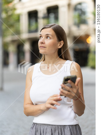 Female pedestrian with phone in summer European capital 136180130