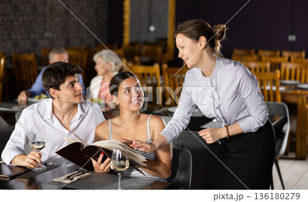 Female owner of restaurant offering dishes from menu to young couple Female owner of restaurant offering dishes from menu to young couple 136180279