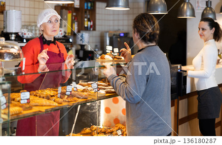 Bakery shop senior female assistant talk to customer, answers questions and recommends fresh products 136180287