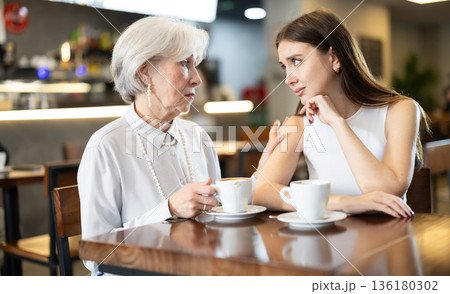 Elderly woman comforts an upset girl while sitting at table in cafe 136180302