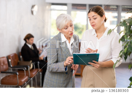 Young female office worker discussing papers with elderly woman Young female office worker discussing papers with elderly woman 136180303