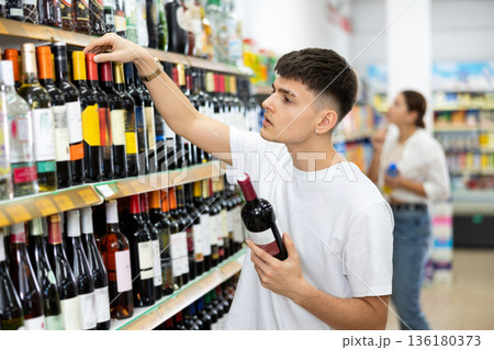 Thoughtful young guy choosing alcoholic drinks in supermarket Thoughtful young guy choosing alcoholic drinks in supermarket 136180373