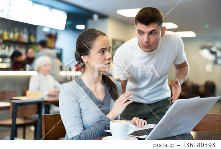 Girl asks her boyfriend not to disturb her while he works on his laptop in cafe Girl asks her boyfriend not to disturb her while he works on his laptop in cafe 136180393