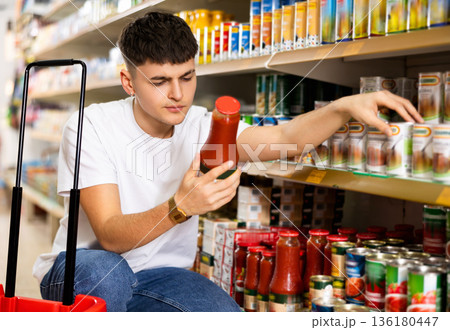 Young man choosing preserved vegetables for himself in supermarket Young man choosing preserved vegetables for himself in supermarket 136180447