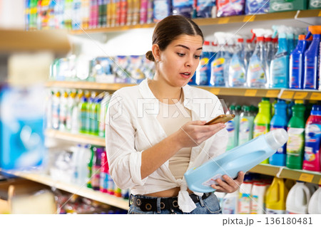 Surprised girl scanning label of detergent with phone in supermarket Surprised girl scanning label of detergent with phone in supermarket 136180481