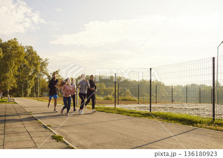 Group of adult runners jogging together in park on sunny day for fitness training outdoors 136180923