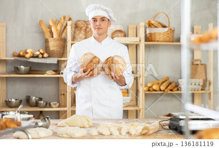 Bakery male employee holds ready made bread of bread in hands 136181119