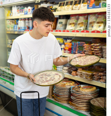 in supermarket in department of semi-finished products, man chooses pizza 136181133