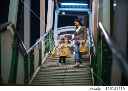 happy mother and child girl with shopping bag enjoying and walking down footbridge stairs in bangkok city at night 136181210