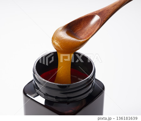 黒いボトルから木のスプーンですくった濃厚なマヌカハニー（白背景・切り抜き素材） 136181639