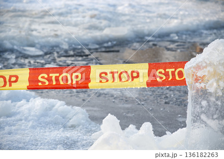 Yellow and red stop tape barrier in icy winter conditions with snow and ice formations 136182263
