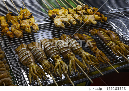 Marinated Squid Skewers On Grill Rack, A sizzling photo of marinated squid , glossy tentacles and charred edges glistening with marinade in grill, for seafood BBQ or street food documentary. 136183528