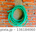 roll of green rubber water hose hangs on a brick wall 136184060