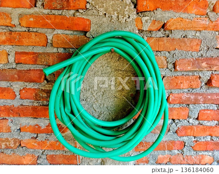 roll of green rubber water hose hangs on a brick wall 136184060