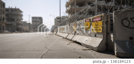 Concrete barricade with razor wire and danger signs on a desolate city street. Military restricted zone warning with skull symbol. Urban conflict checkpoint background 136184123