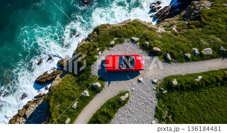 Aerial View Of Red Convertible On Coastal Path Next To Blue Ocean And Green Landscape 136184481