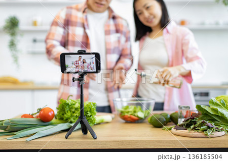 A couple films a cooking video in their kitchen, preparing a fresh salad with healthy ingredients 136185504