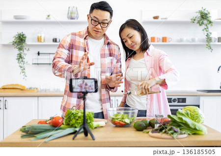 An Asian couple is preparing a salad in their kitchen while recording a video for their followers 136185505