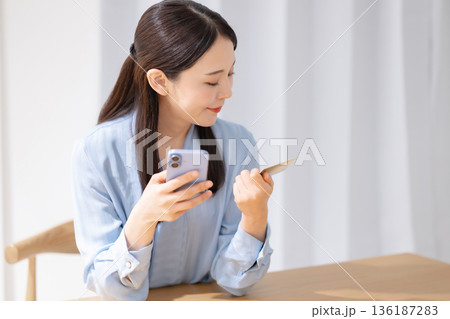 クレジットカードを見ながらスマホを操作する女性 クレジットカードを見ながらスマホを操作する女性 136187283