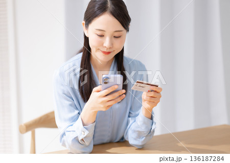クレジットカードを見ながらスマホを操作する女性 クレジットカードを見ながらスマホを操作する女性 136187284