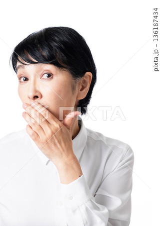 口を手で隠すショートヘアーの白いシャツを着たシニア女性 136187434
