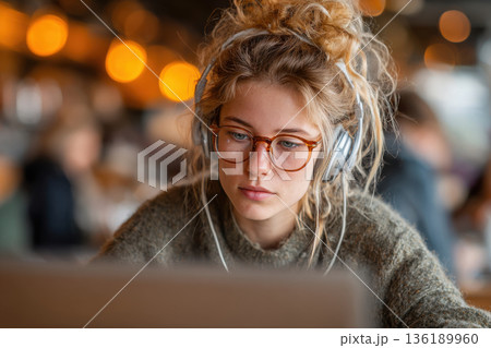 A young woman, a student or freelancer, works on a laptop with headphones 136189960