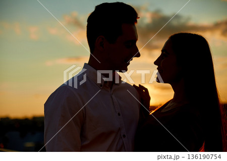 Couple enjoys sunset while sharing a moment on a rooftop in the evening sky Couple enjoys sunset while sharing a moment on a rooftop in the evening sky 136190754
