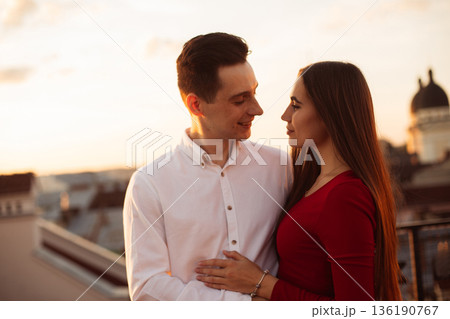 Couple stands together on rooftop during sunset, sharing a moment in the evening light Couple stands together on rooftop during sunset, sharing a moment in the evening light 136190767