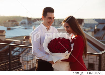 Couple exchanges a bouquet of roses on a rooftop at sunset in an urban setting 136190779