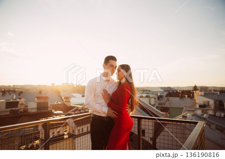 Couple enjoys time together on a rooftop at sunset in a city setting during warm weather Couple enjoys time together on a rooftop at sunset in a city setting during warm weather 136190816