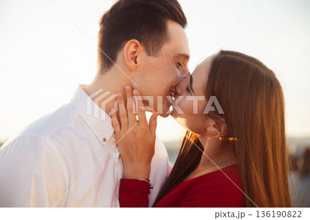 Couple kisses during sunset on a rooftop while enjoying a moment together in the warm evening light Couple kisses during sunset on a rooftop while enjoying a moment together in the warm evening light 136190822