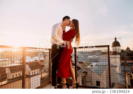 Couple kisses on rooftop during sunset over city buildings in evening light 136190824