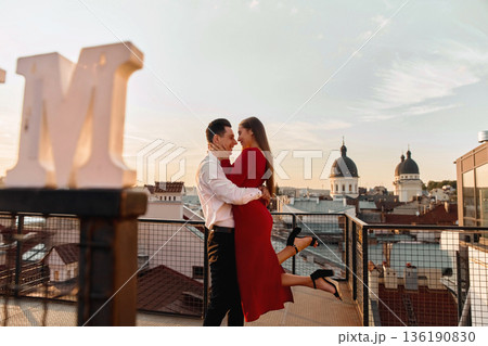 Couple dancing on the rooftop during sunset in a city setting with historic buildings and a clear sky 136190830