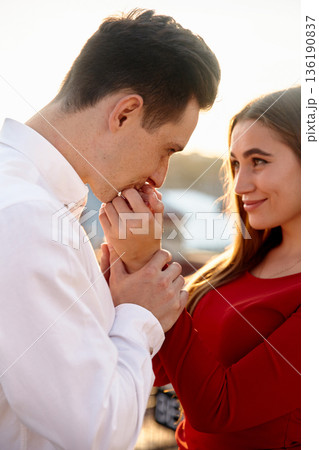 Couple sharing a moment together near water during sunset while engaged in a tender gesture of affection Couple sharing a moment together near water during sunset while engaged in a tender gesture of affection 136190837