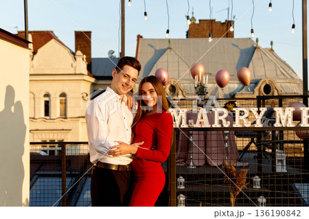 Couple stands together on rooftop with decorations for engagement proposal during sunset in city Couple stands together on rooftop with decorations for engagement proposal during sunset in city 136190842
