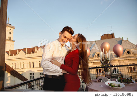 Couple enjoys time together on rooftop during sunset while sharing food and drinks in the city 136190995