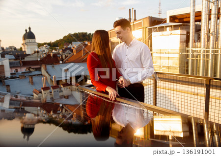 Couple enjoys a sunset on a rooftop in a city with historical buildings and vibrant sky Couple enjoys a sunset on a rooftop in a city with historical buildings and vibrant sky 136191001