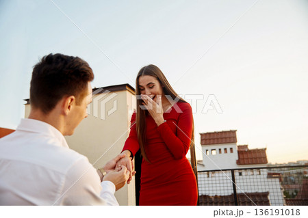 Couple celebrates engagement on rooftop at sunset with joyful emotions and surprise in the air 136191018