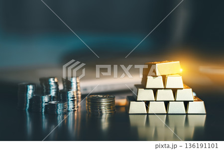 Stack of gold bars and piles of silver coins on dark office desk. Concept of wealth management, safe haven investment, financial stability, and capital growth. Stack of gold bars and piles of silver coins on dark office desk. Concept of wealth management, safe haven investment, financial stability, and capital growth. 136191101