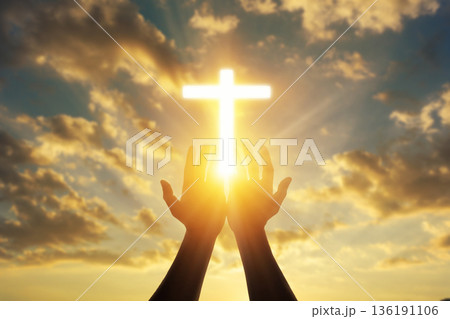 Human hands open palm up worshiping a glowing Christian cross in sunset sky. Concept for faith, spirituality, and hope. 136191106